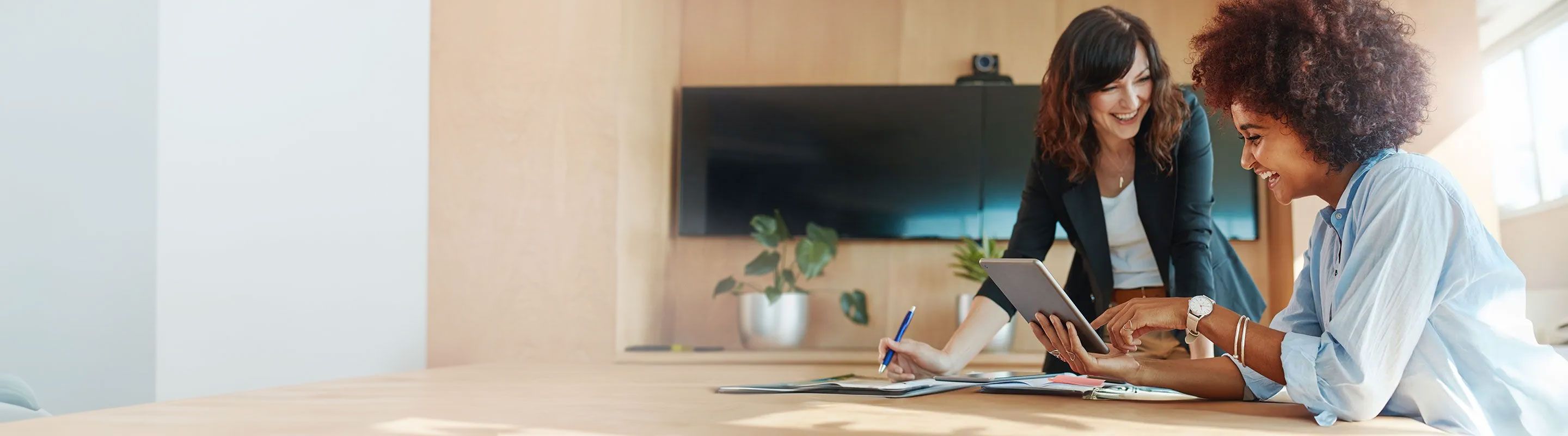 Two women at a table with a tablet, collaborating to enhance leadership and CX skills.